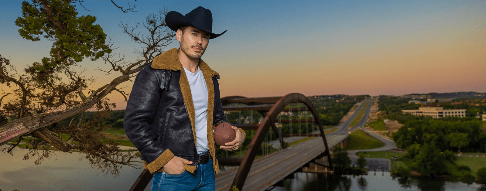 Man in cowboy hat stands in front of bridge